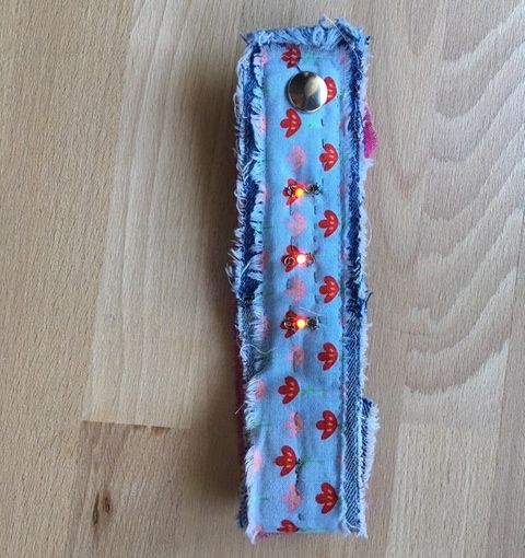 Selbst genähtes Armband aus Jeansstoff mit geblümtem Band, in das drei leuchtende LEDs eingenäht sind
