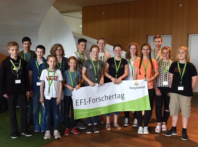 Jugendliche mit Namensschildern und grünen Bändern halten ein Banner mit der Aufschrift EFI-Forschertag