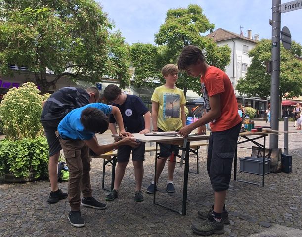 Vier Jugendliche arbeiten an einem Klapptisch mitten in der Fußgängerzone an ihrem Versuch