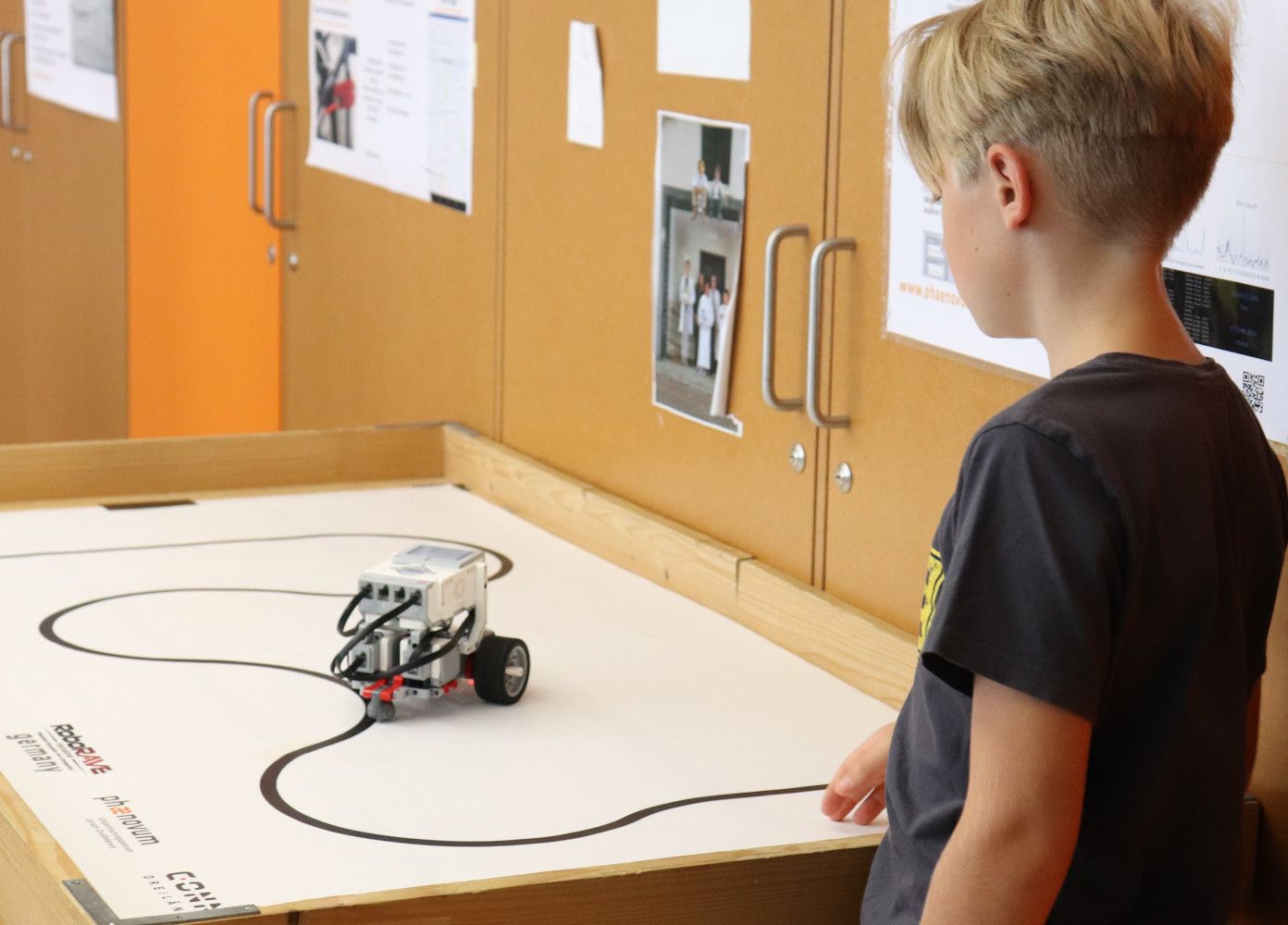 Ein Junge beobachtet, wie sein Lego-Mindstorms-Roboter der schwarzen Linie auf der Wettbewerbsplatte folgt