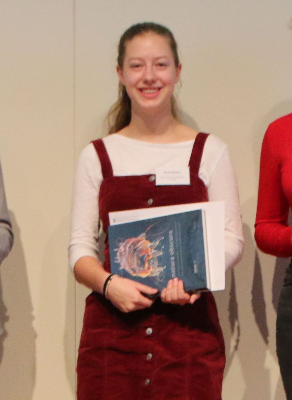 Eine junge Frau mit Namensschild hält lächelnd das Buch, das sie als Preis bekommen hat