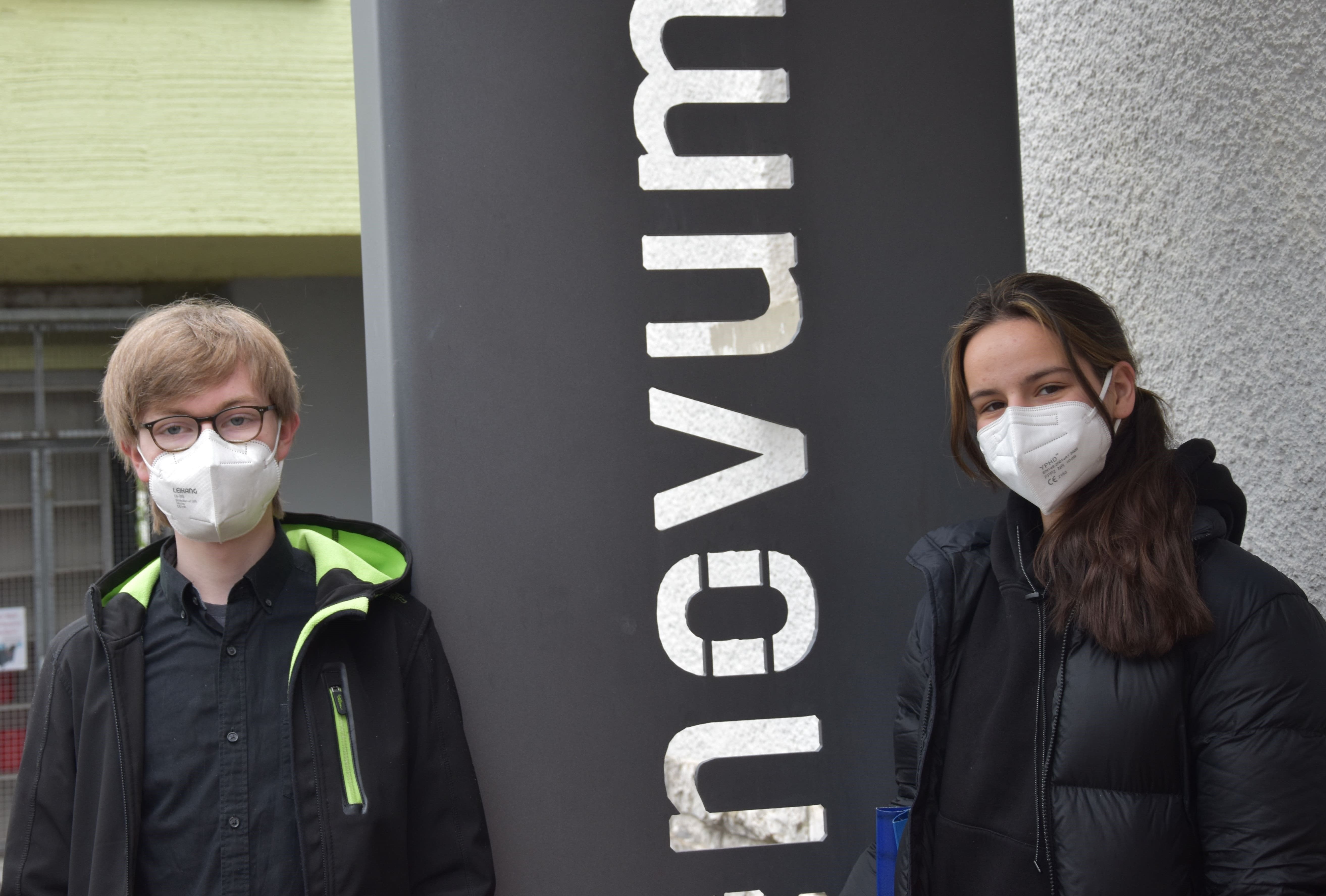 Zwei Jugendliche mit FFP2-Maske stehen neben der Stele mit dem phænovum-Schriftzug