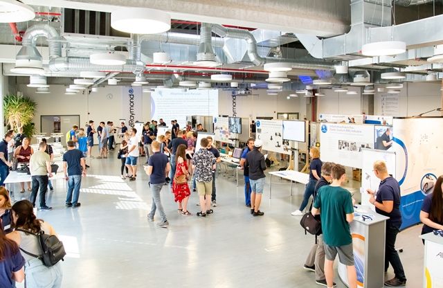 Besucherinnen und Besucher gehen durch eine helle Halle zwischen Ausstellungstafeln und Mitmachstationen