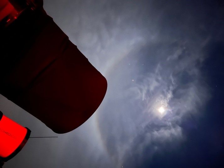 Der Mond mit Halo in dünnen Wolken, im Vordergrund die Silhouette eines Teleskops im roten Licht