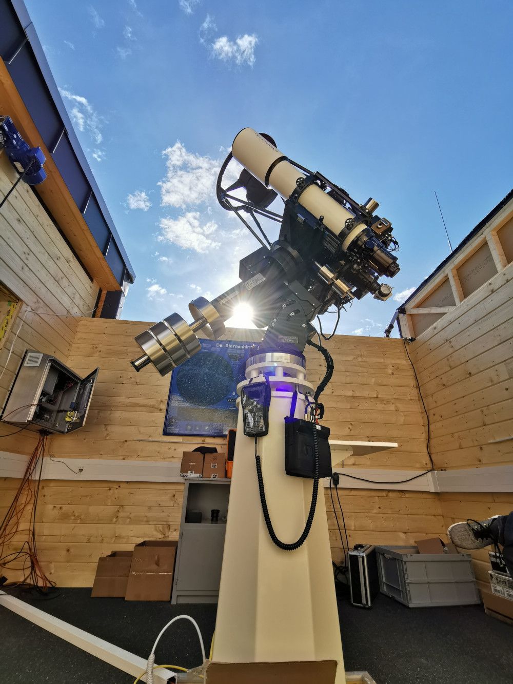 Das Teleskop der Sternwarte steht bei geöffnetem Dach unter blauem Himmel, die Sonne blitzt hinter dem Tubus hervor