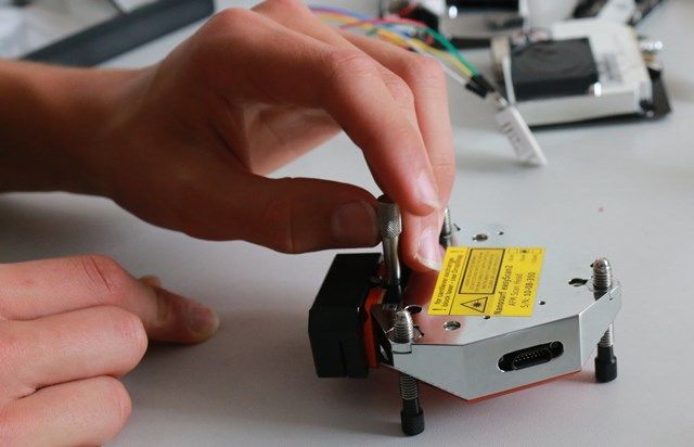 Zwei Hände justieren ein Lasermodul mit gelbem Warnaufkleber auf seiner Halterung
