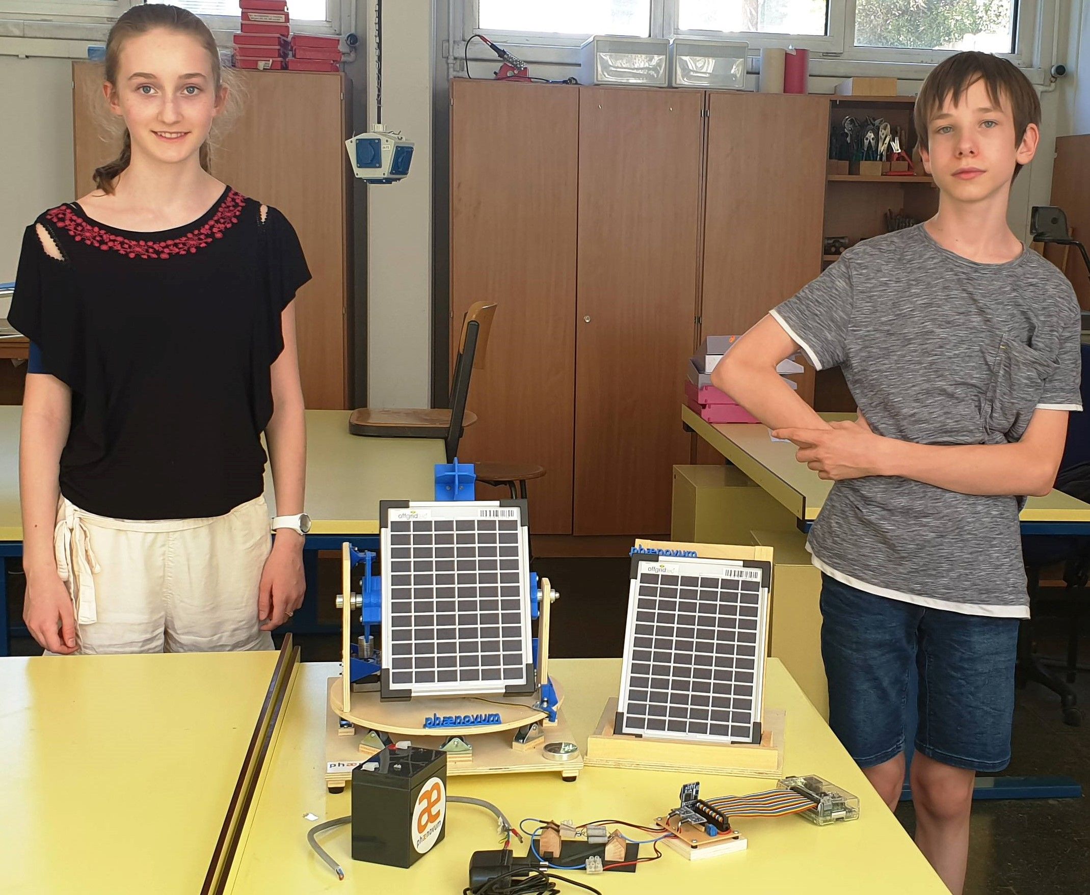 Zwei Jugendliche stehen neben ihrer selbst gebauten Nachführung mit zwei Solarmodulen auf der Werkbank