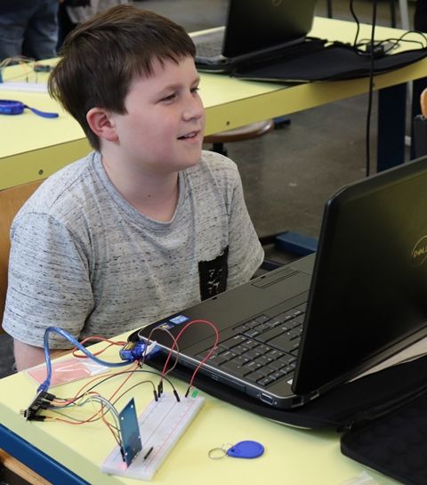 Ein Junge sitzt lachend vor seinem Laptop, daneben eine Steckplatine mit LEDs und ein RFID-Chip