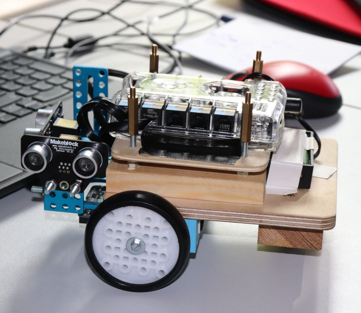 Ein mBot-Roboter mit selbst gebautem Holzaufbau und Ultraschallsensor steht neben einem Laptop