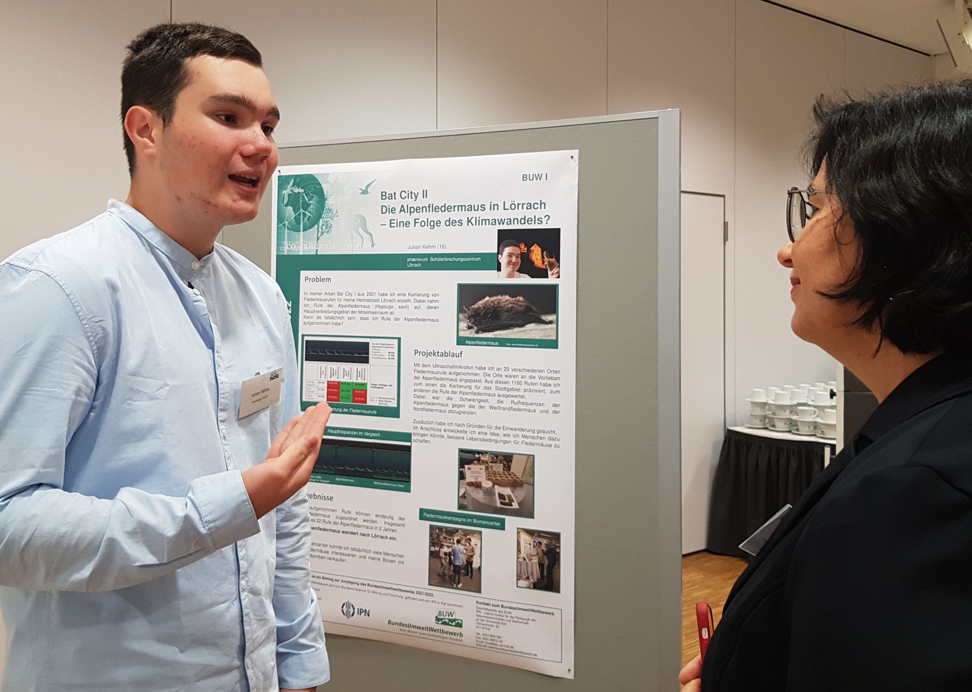Ein Jugendlicher erklärt einer Zuhörerin sein Projektplakat über die Alpenfledermaus in Lörrach