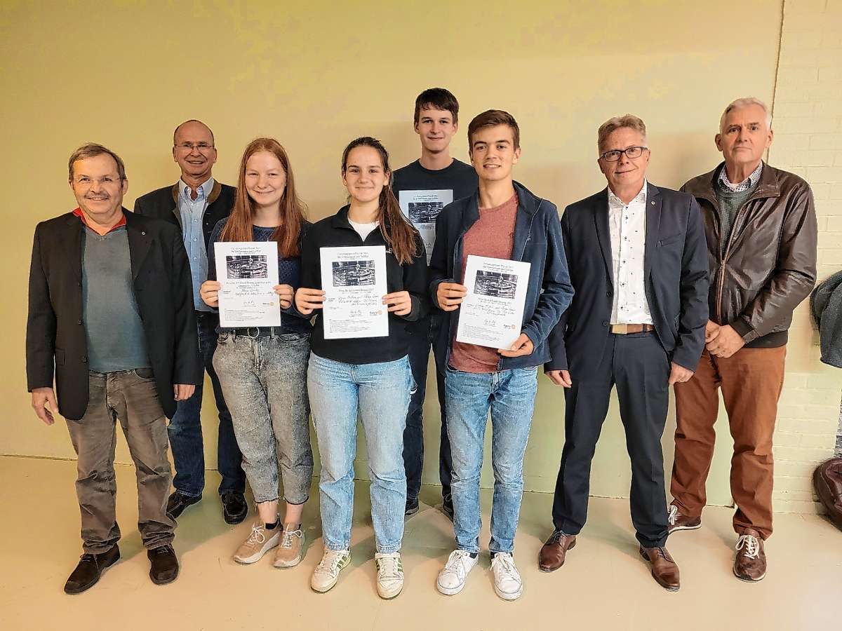 Drei Jugendliche zeigen ihre Urkunden in die Kamera, links und rechts von ihnen stehen mehrere Erwachsene
