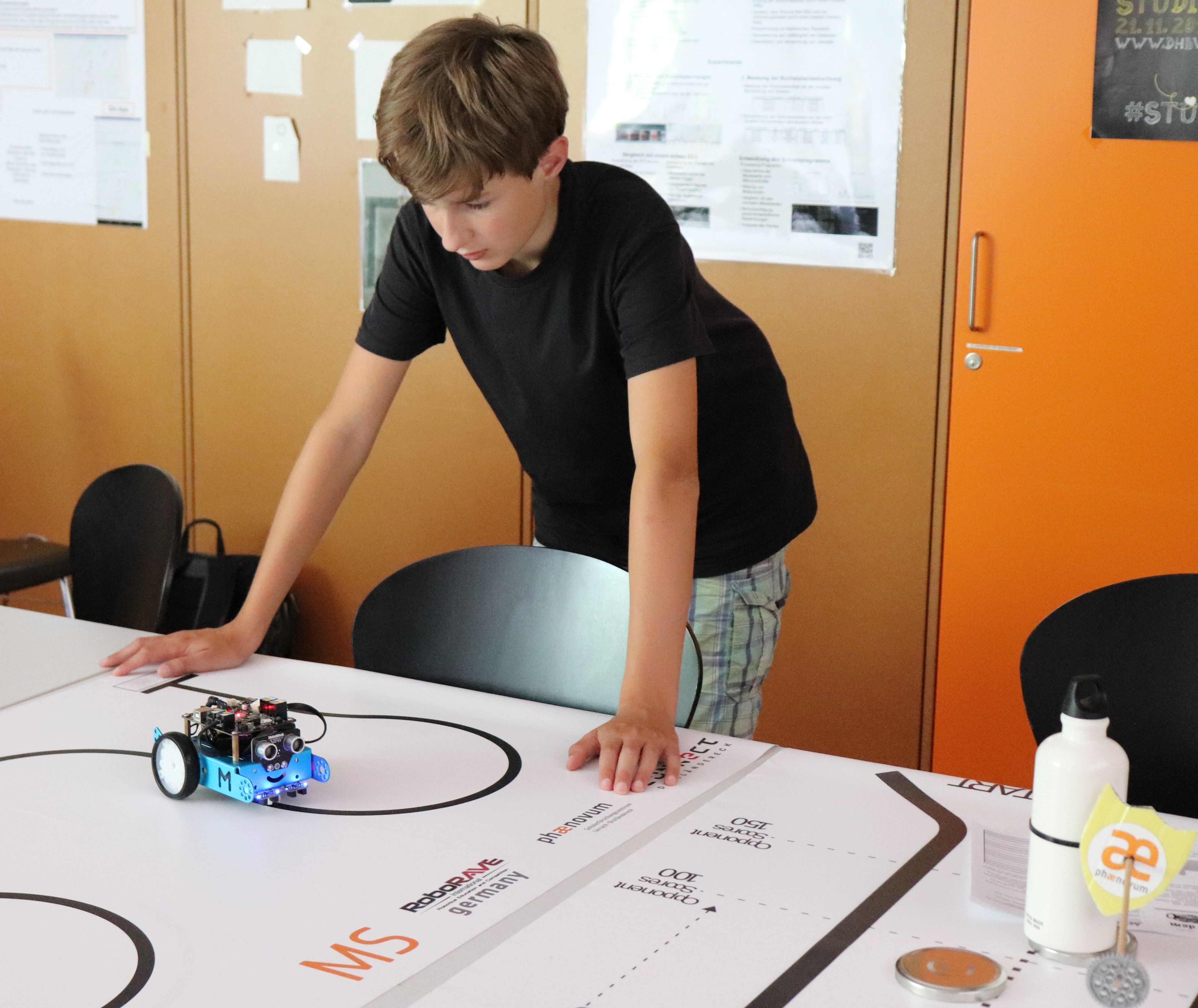 Ein Junge beugt sich über die Wettbewerbsmatte und beobachtet seinen mBot auf der schwarzen Linie
