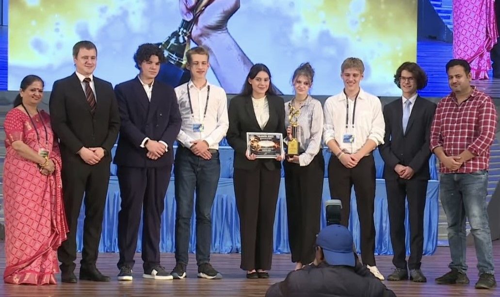 Auf der Bühne einer internationalen Veranstaltung nimmt das Team eine Plakette und einen goldenen Pokal entgegen