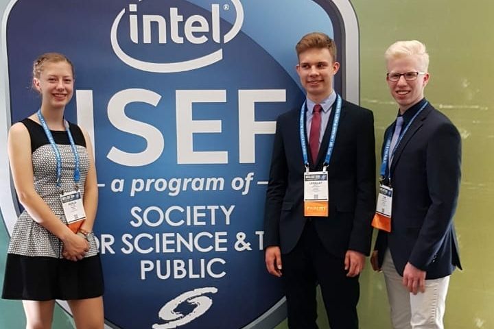 Drei Jugendliche mit Teilnehmerausweisen stehen vor der Wand des Intel ISEF