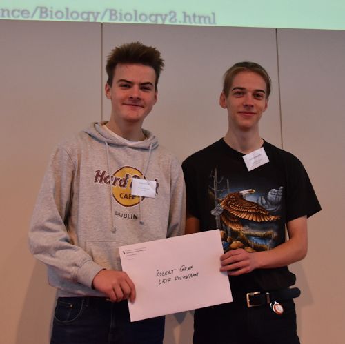 Zwei Jugendliche halten nach der Preisverleihung gemeinsam einen beschrifteten Umschlag in die Kamera