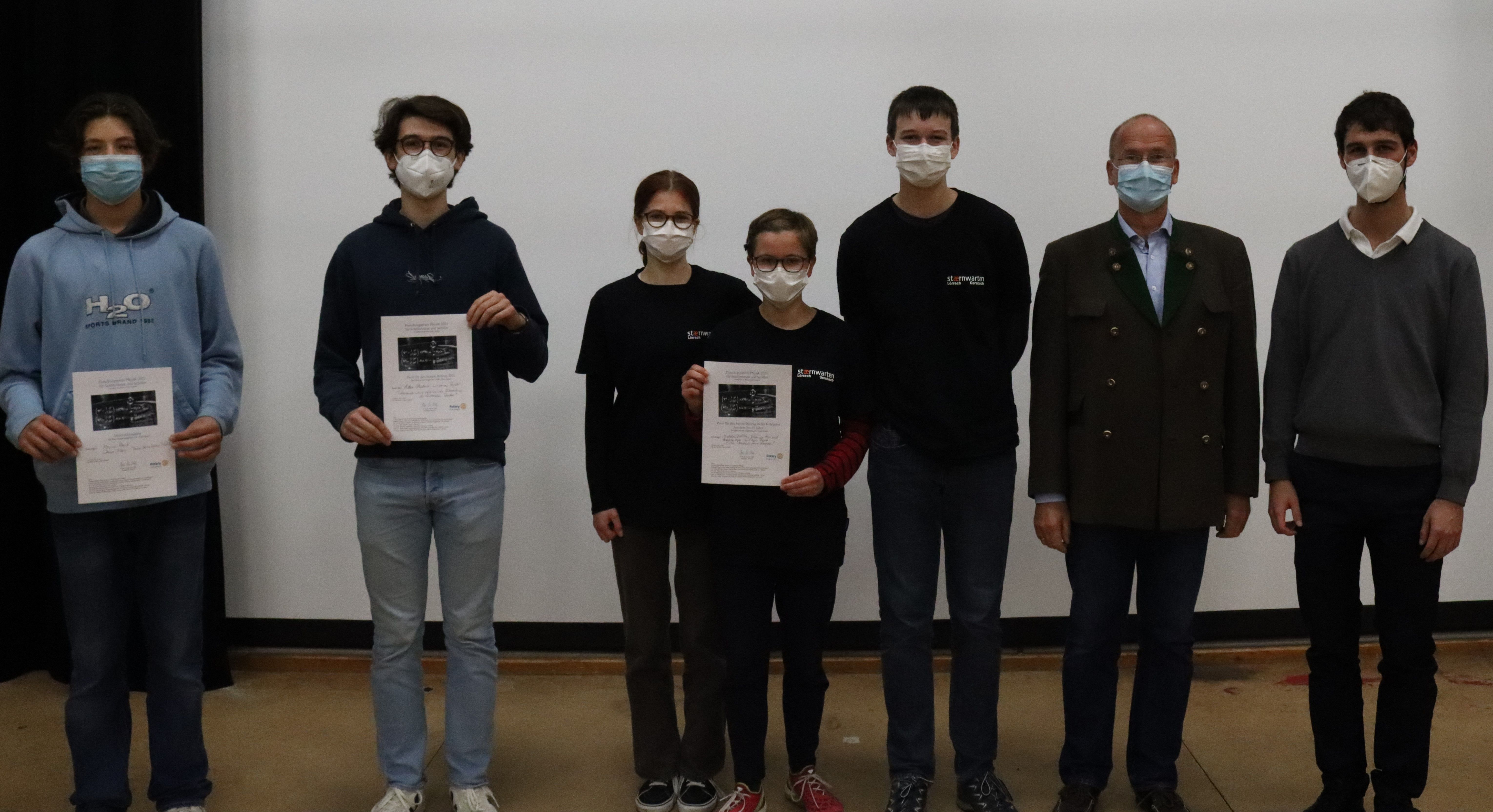 Jugendliche mit Mund-Nasen-Schutz halten ihre Urkunden in die Kamera, rechts neben ihnen zwei Erwachsene