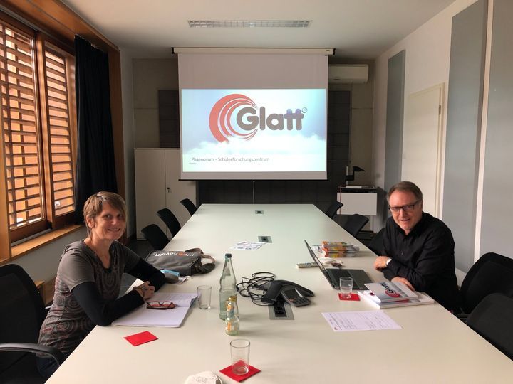 Zwei Personen sitzen im Besprechungsraum am langen Tisch, auf der Leinwand läuft eine Präsentation mit dem Logo der Firma Glatt