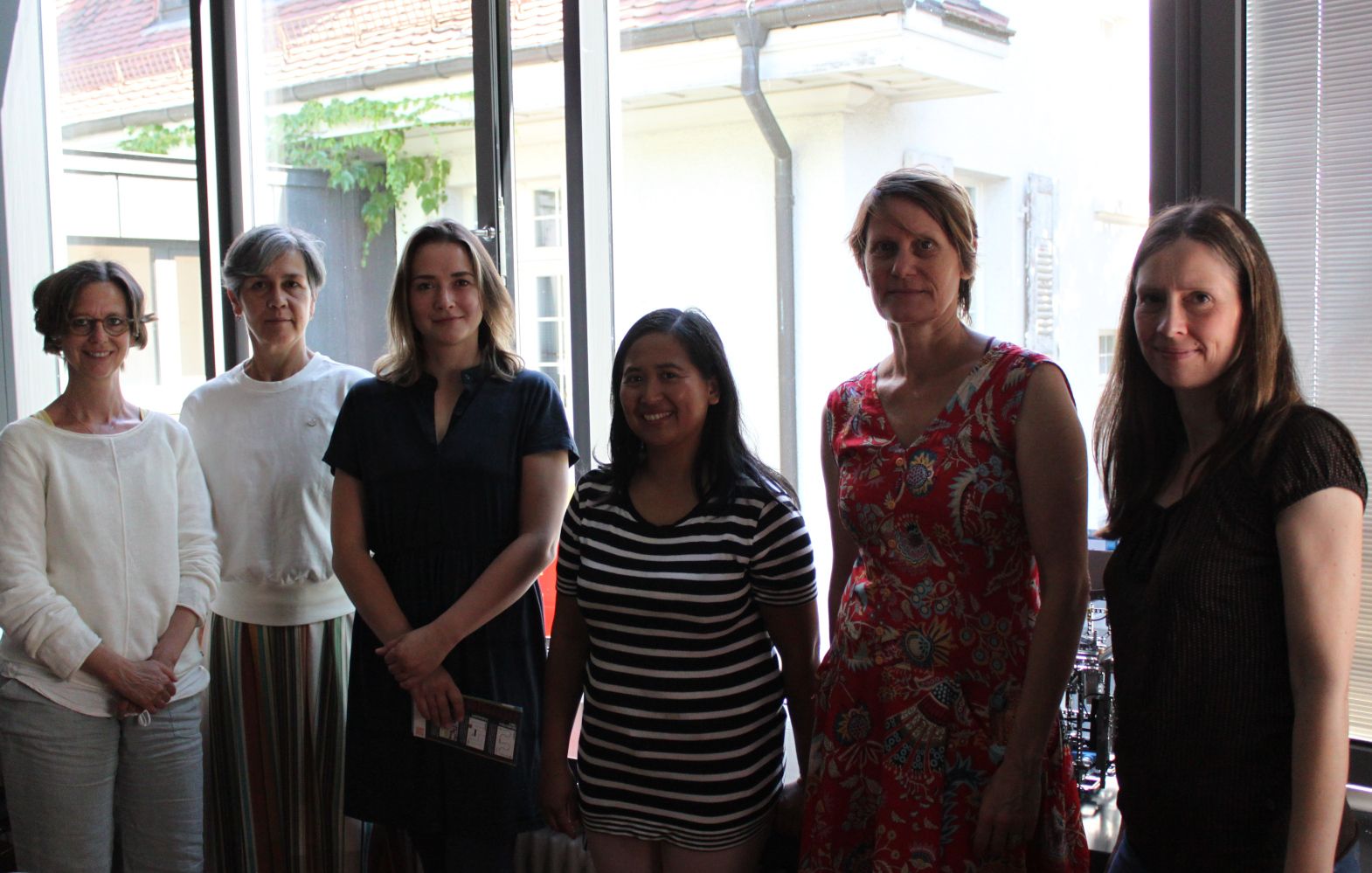 Sechs Frauen stehen nebeneinander vor einer großen Fensterfront